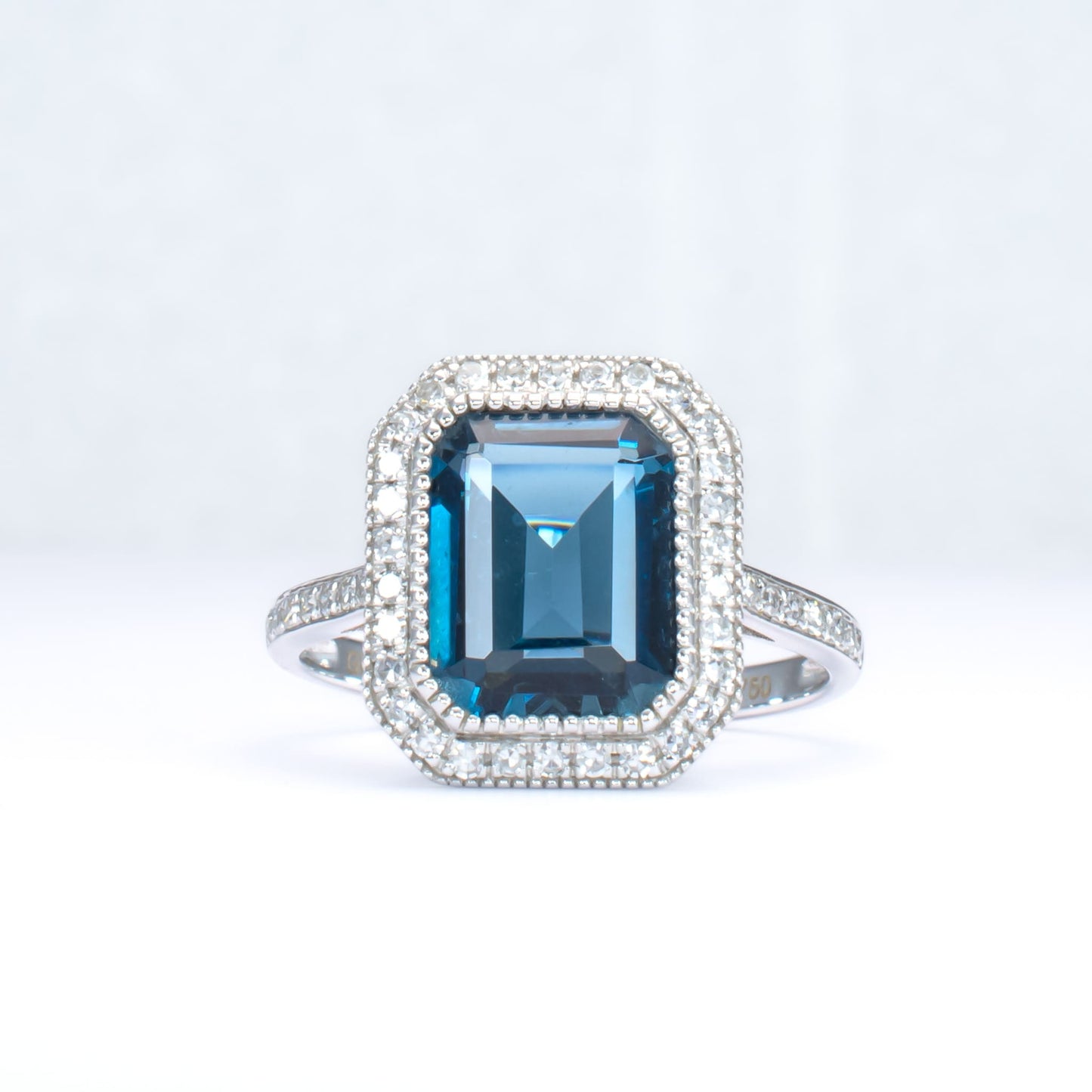 White gold ring with London blue topaz and diamond halo in light gray background