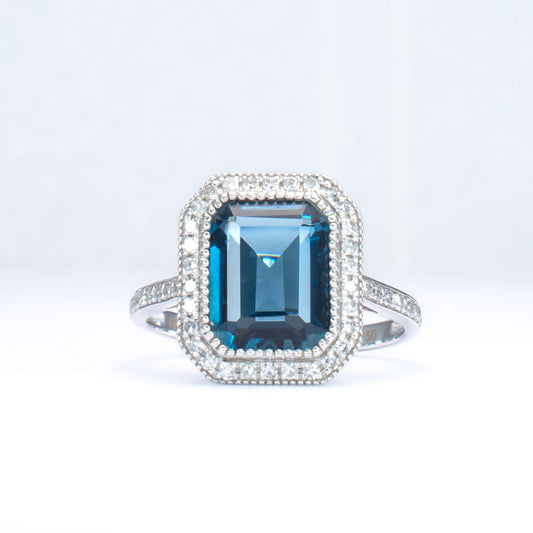 White gold ring with London blue topaz and diamond halo in light gray background