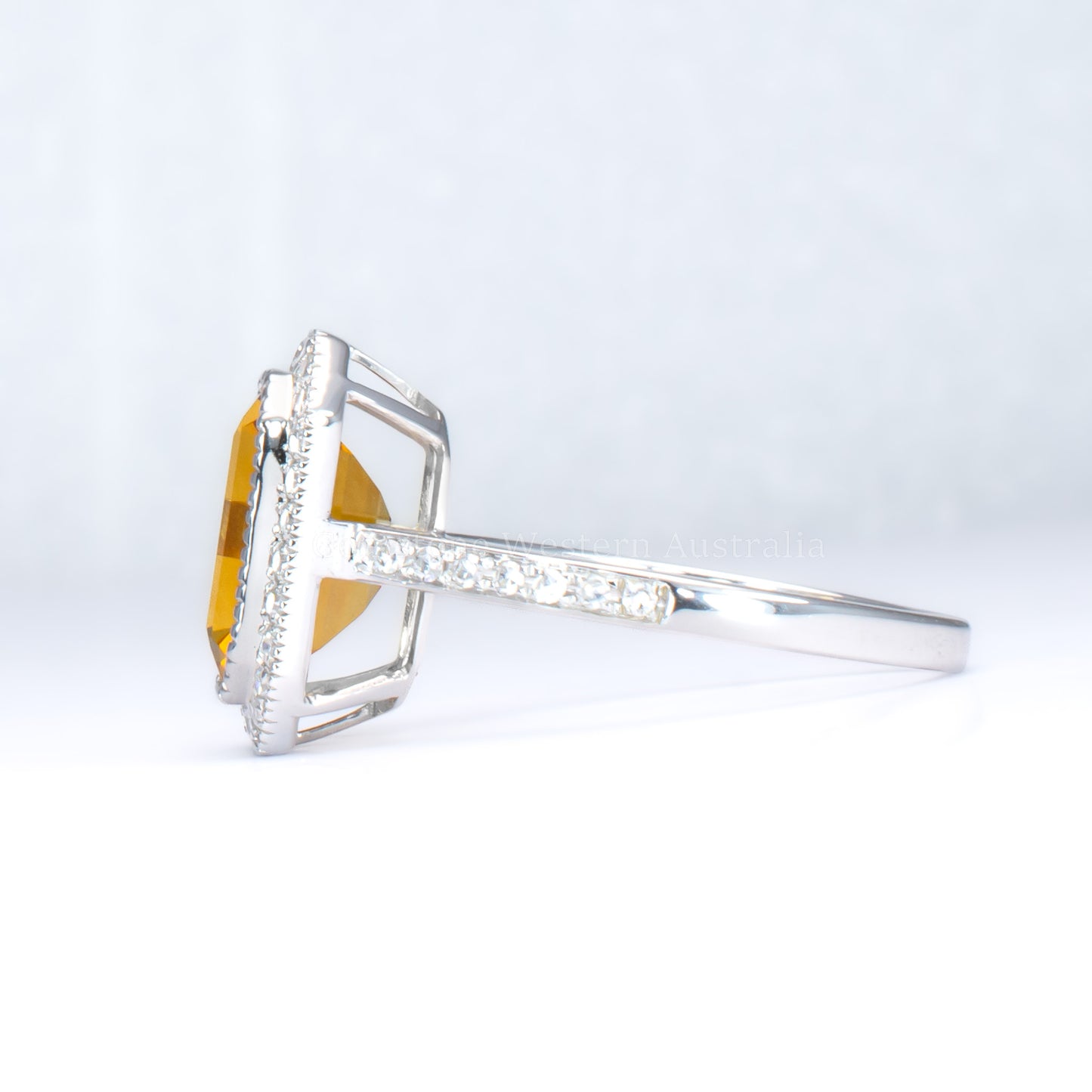 side view of Citrine and diamond halo ring in 18K white gold in light gray background