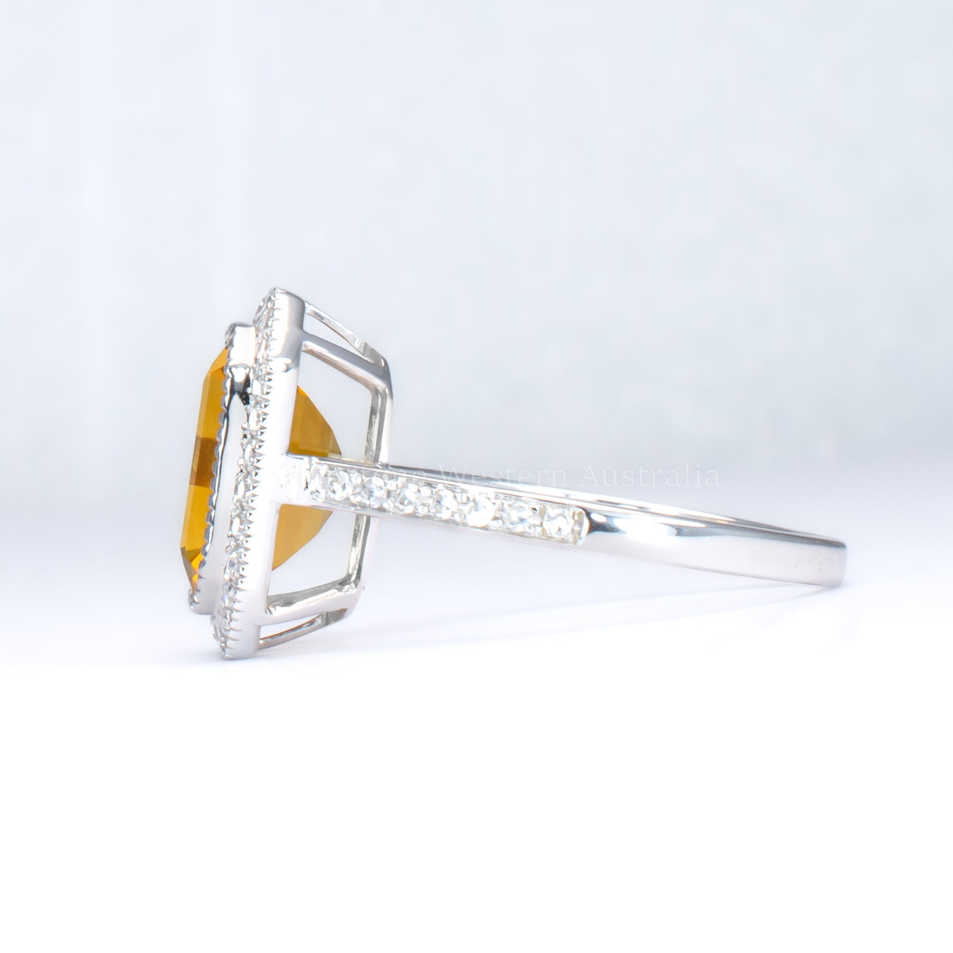 side view of Citrine and diamond halo ring in 18K white gold in light gray background