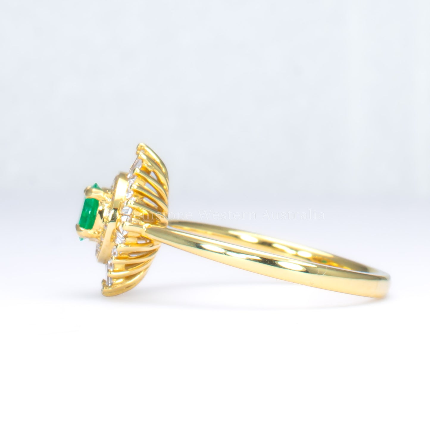 side perspective of emerald Art Deco ring with diamond halo in light gray background