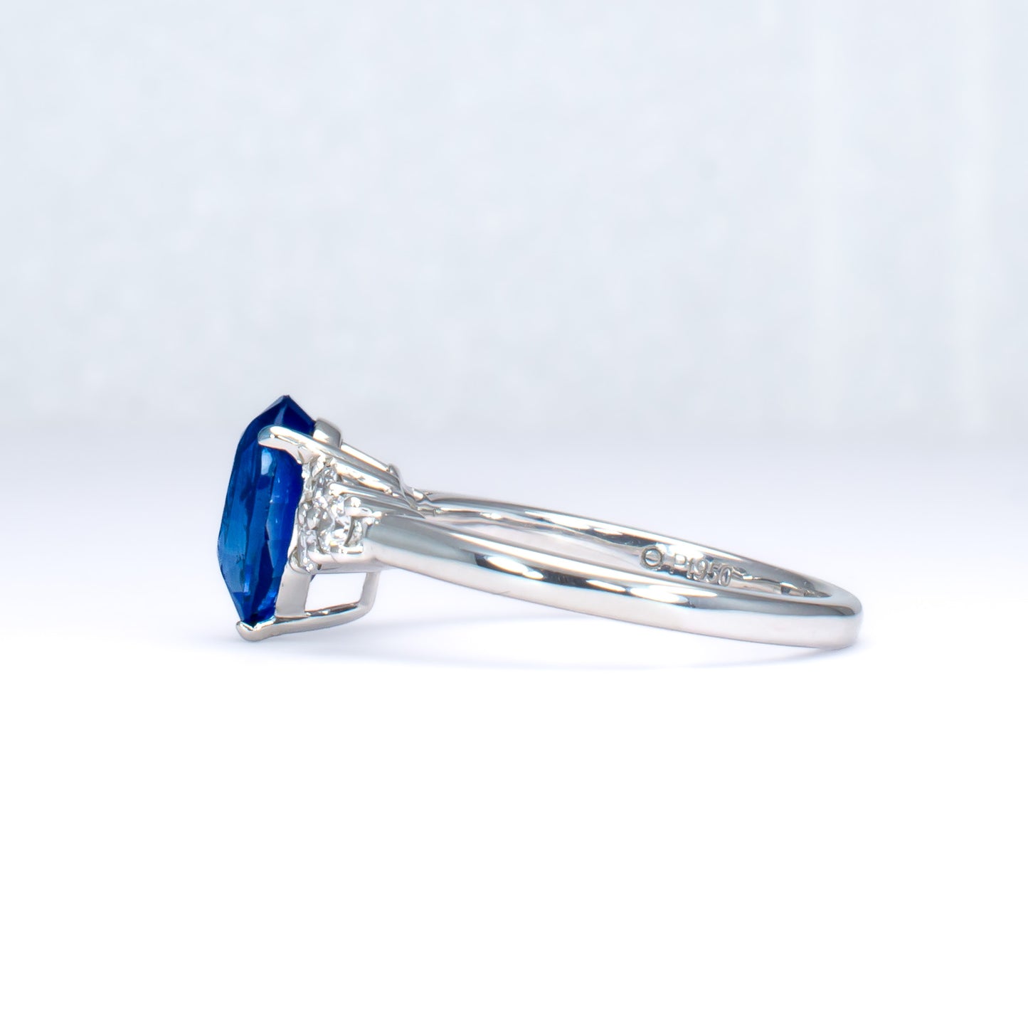 side view of Platinum ring with a blue teardrop-shaped sapphire and smaller diamonds on a light gray background