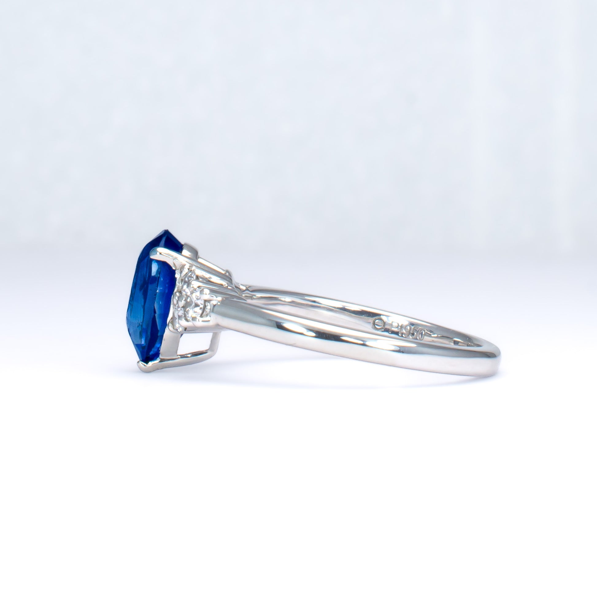 side view of Platinum ring with a blue teardrop-shaped sapphire and smaller diamonds on a light gray background