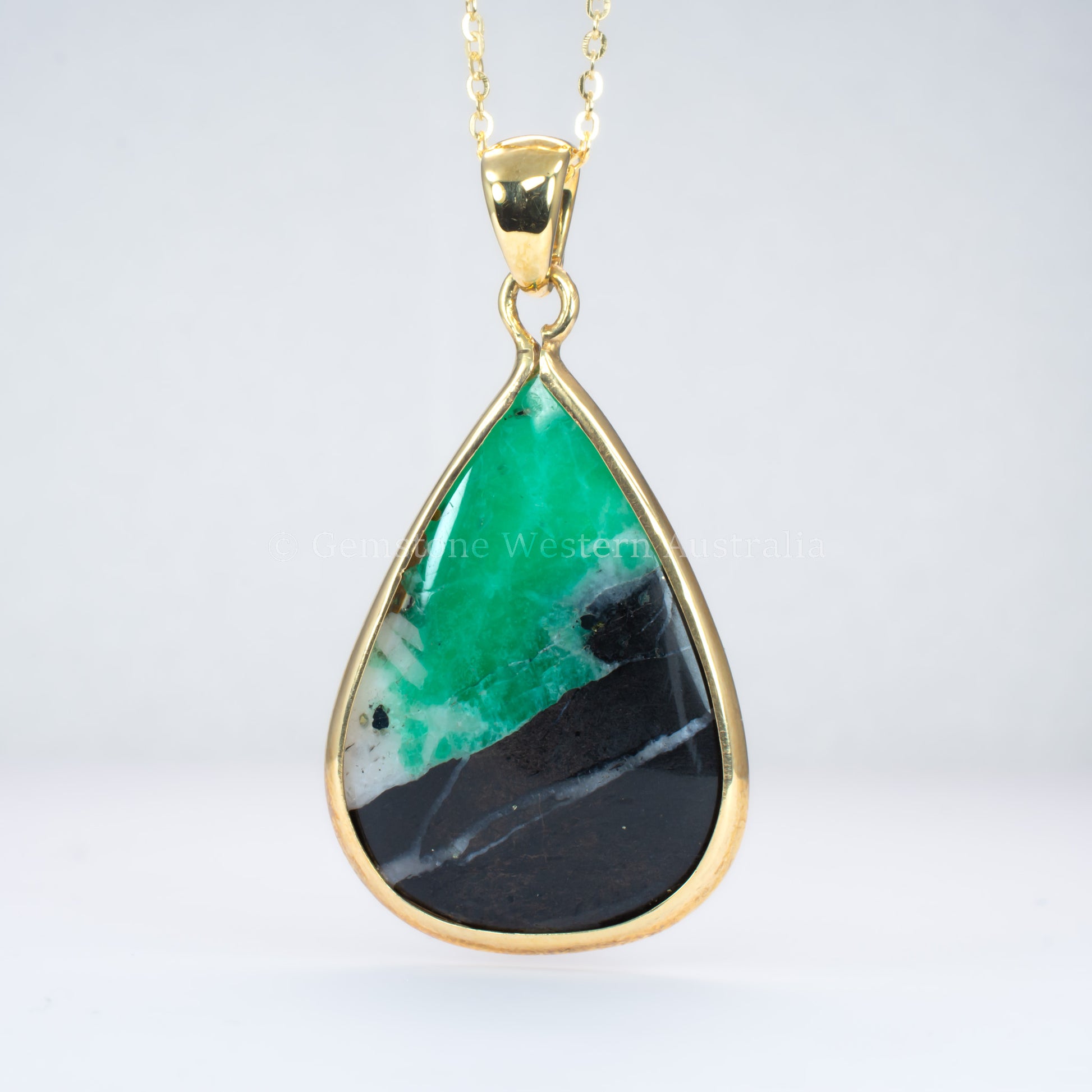 emerald in matrix gold pendant on light gray background
