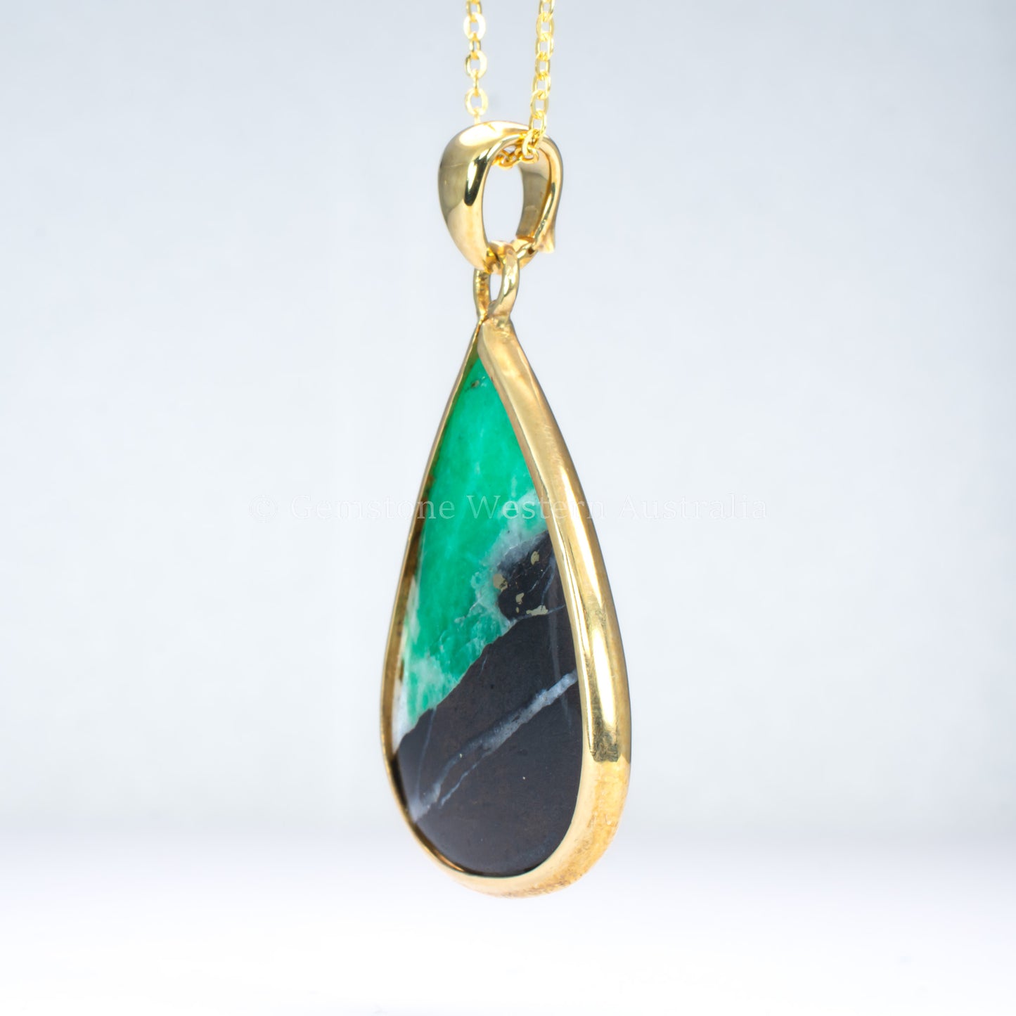 side view of emerald in matrix gold pendant on light gray background