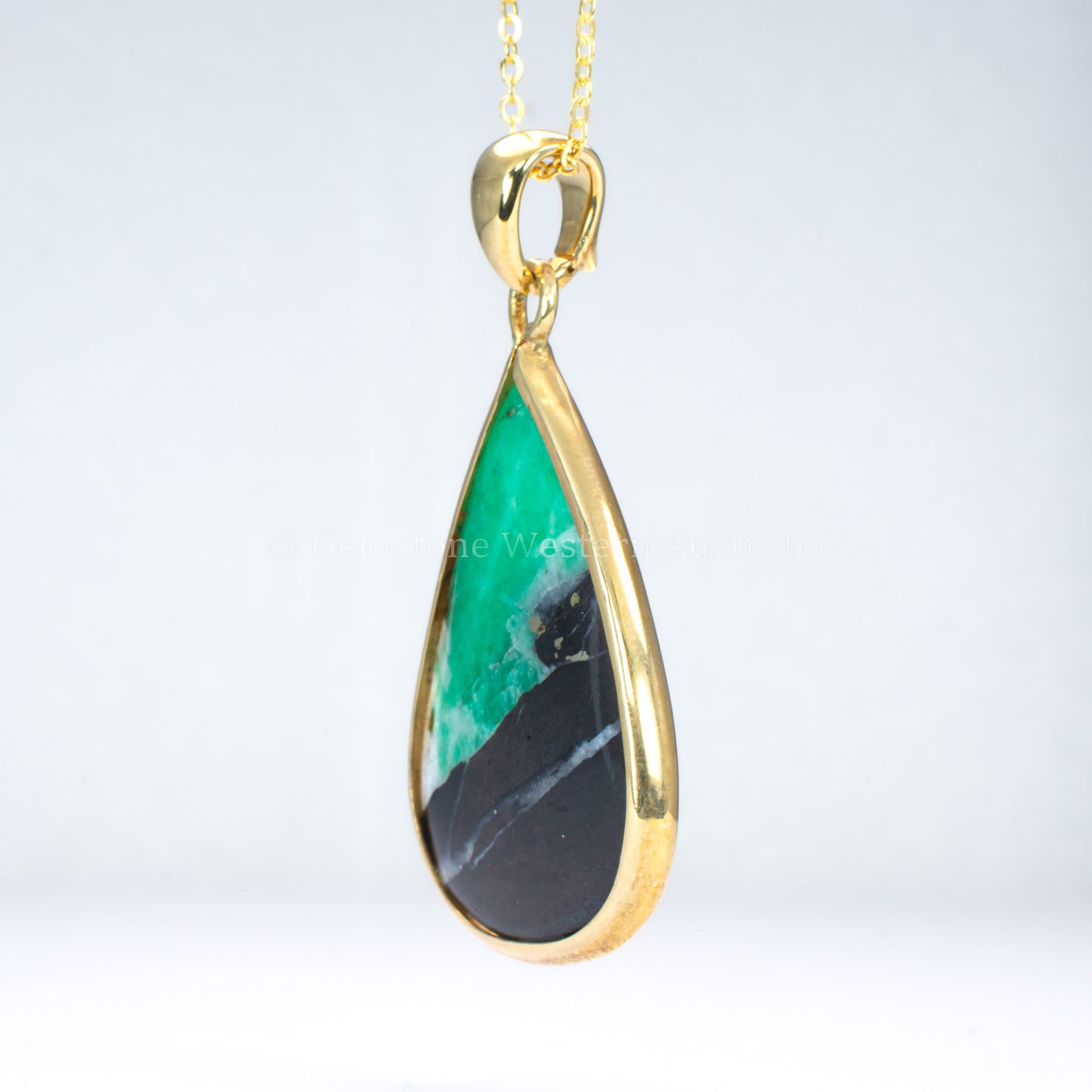 side view of emerald in matrix gold pendant on light gray background