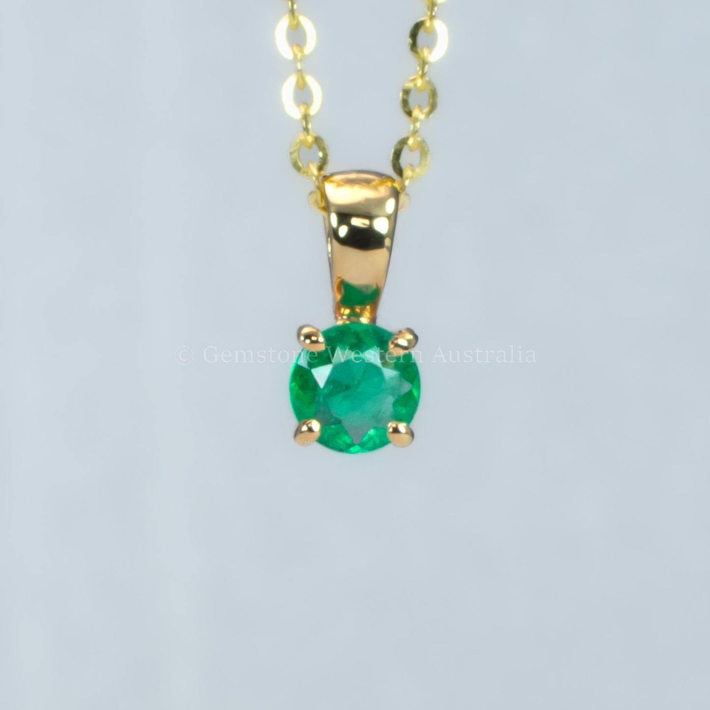 petite emerald pendant in gold in gray background 