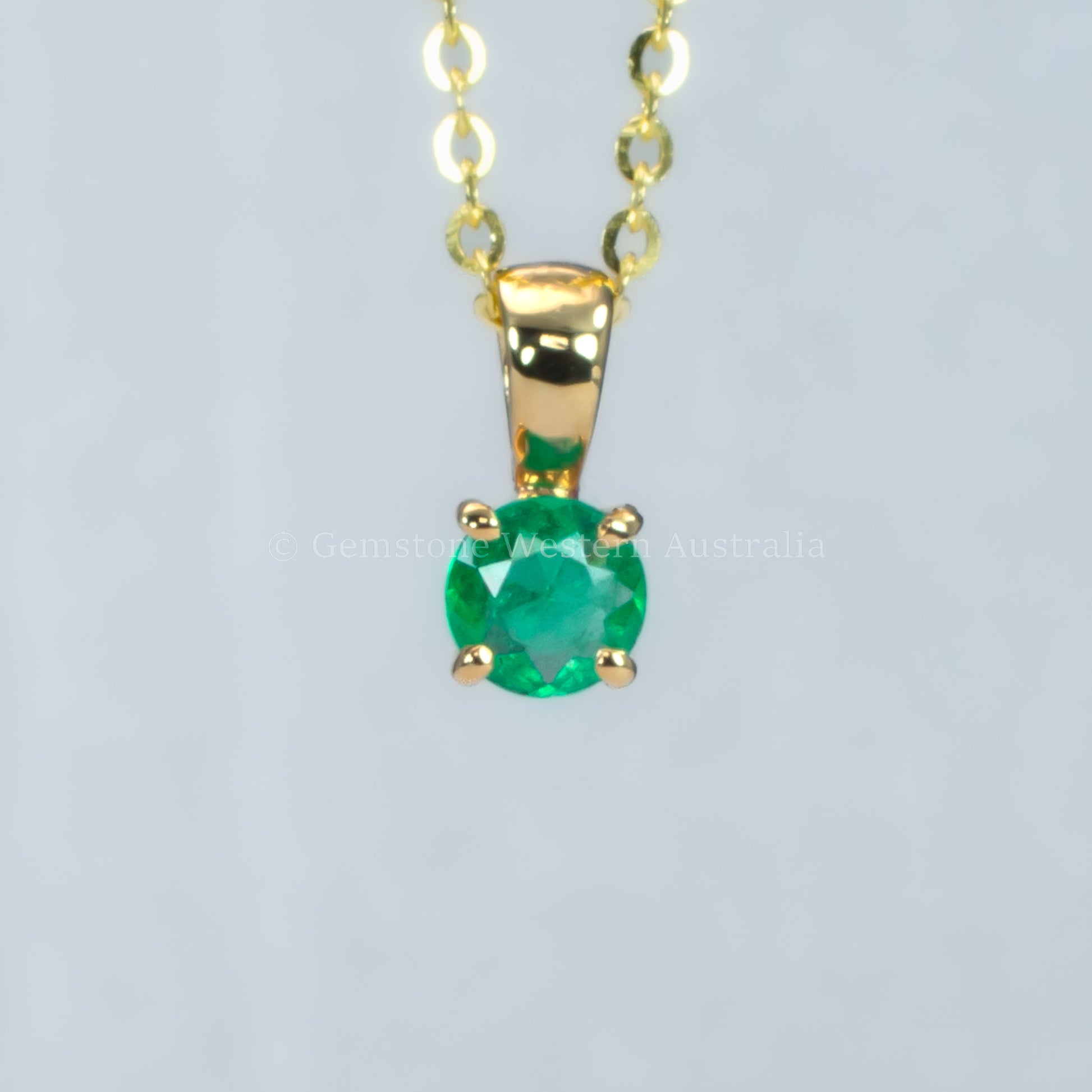 petite emerald pendant in gold in gray background 