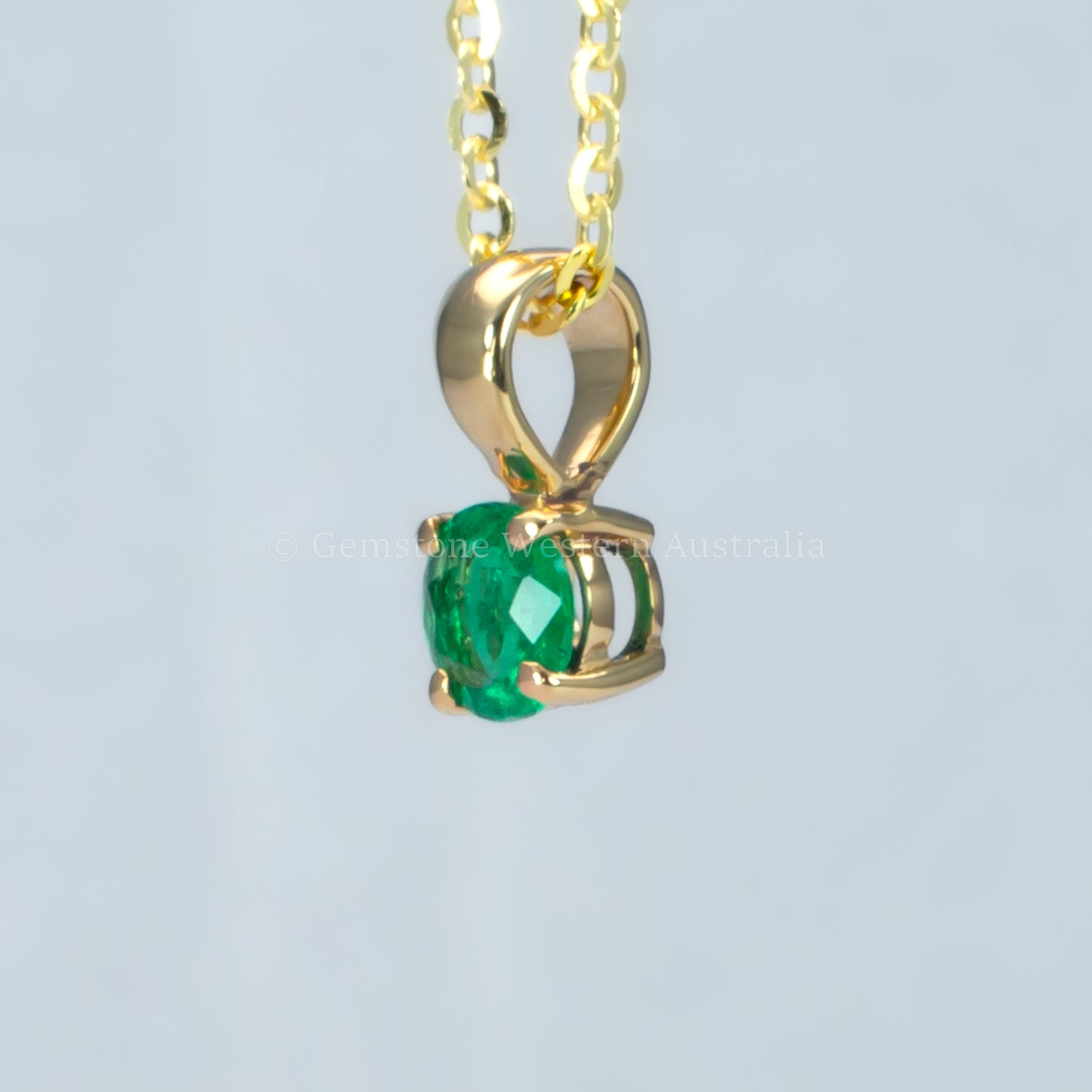 side view of petite emerald pendant in gold in gray background 