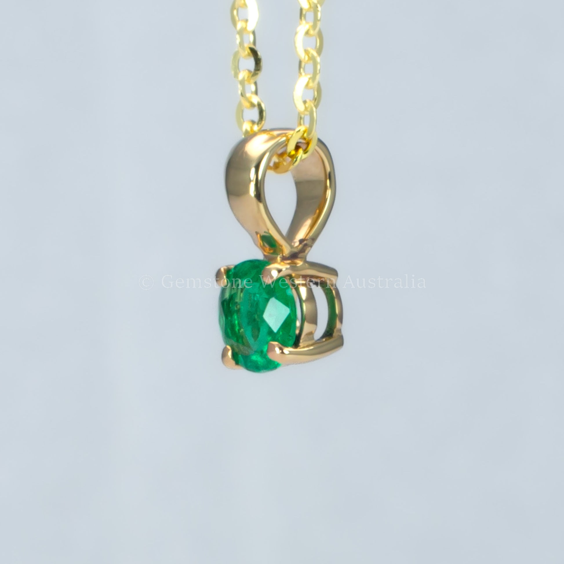 side view of petite emerald pendant in gold in gray background 