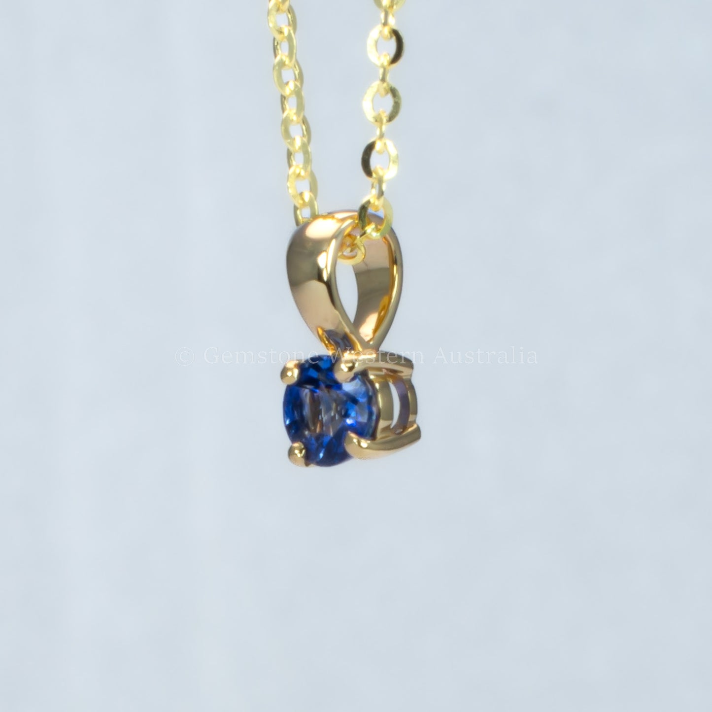 side view of yellow gold royal blue sapphire pendant in gray background