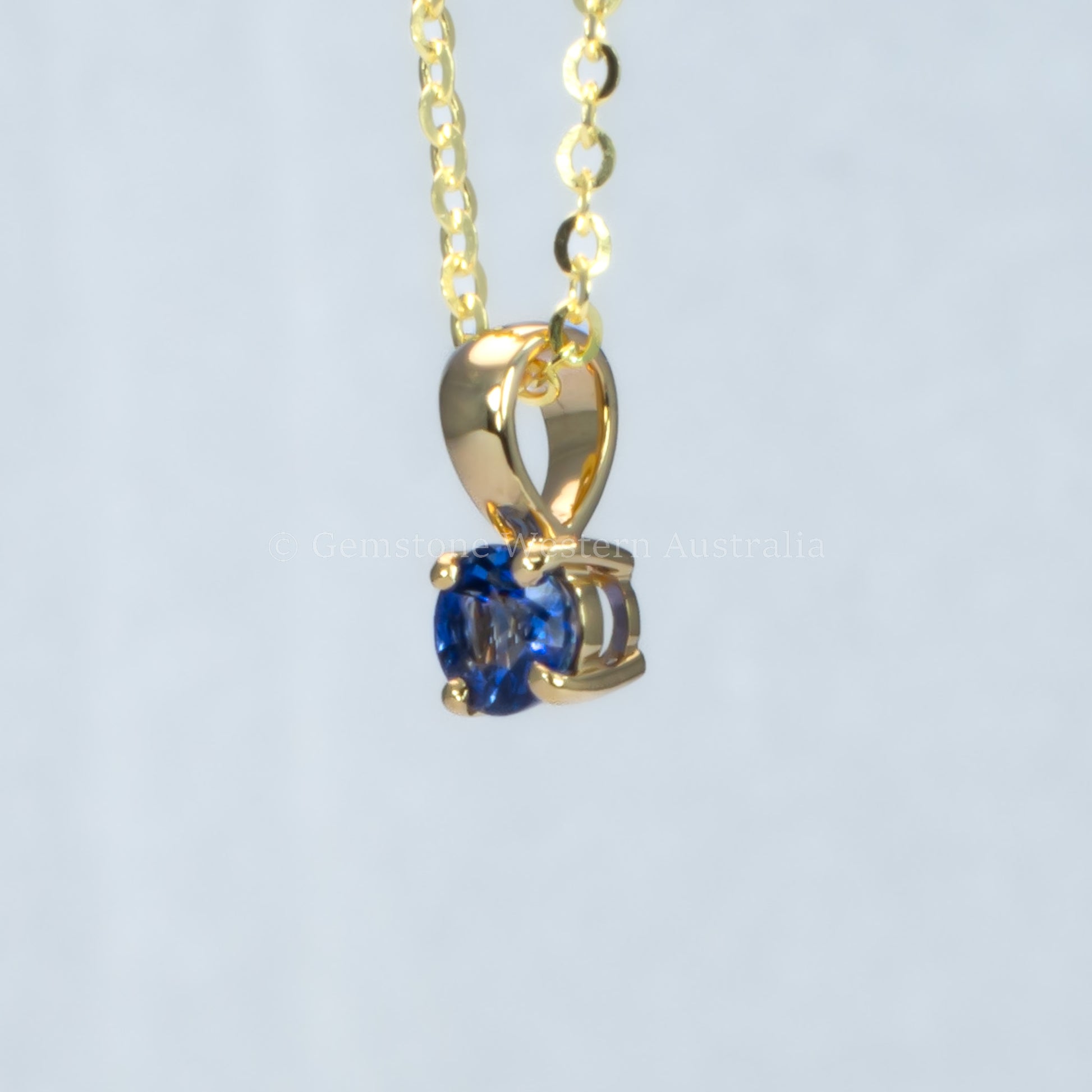 side view of yellow gold royal blue sapphire pendant in gray background