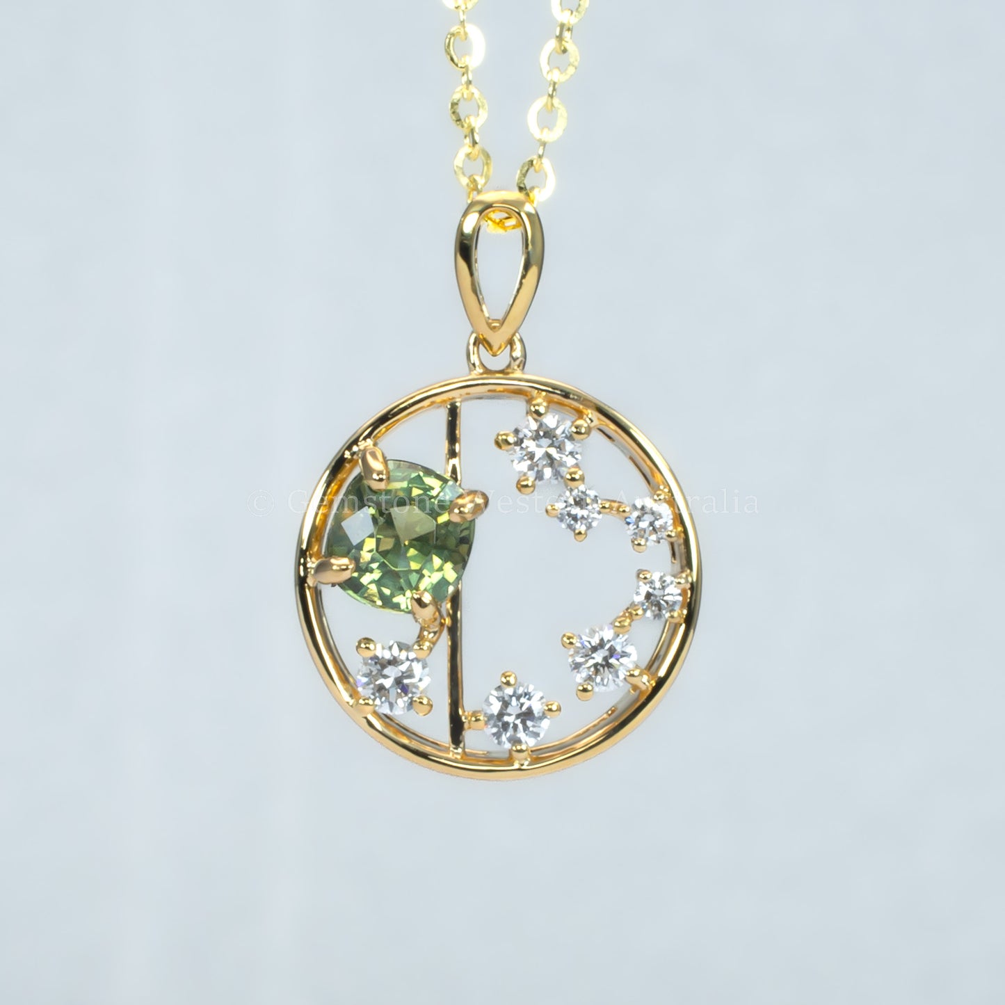 Open circle gold pendant with alexandrite gemstone and small diamonds on a light gray background