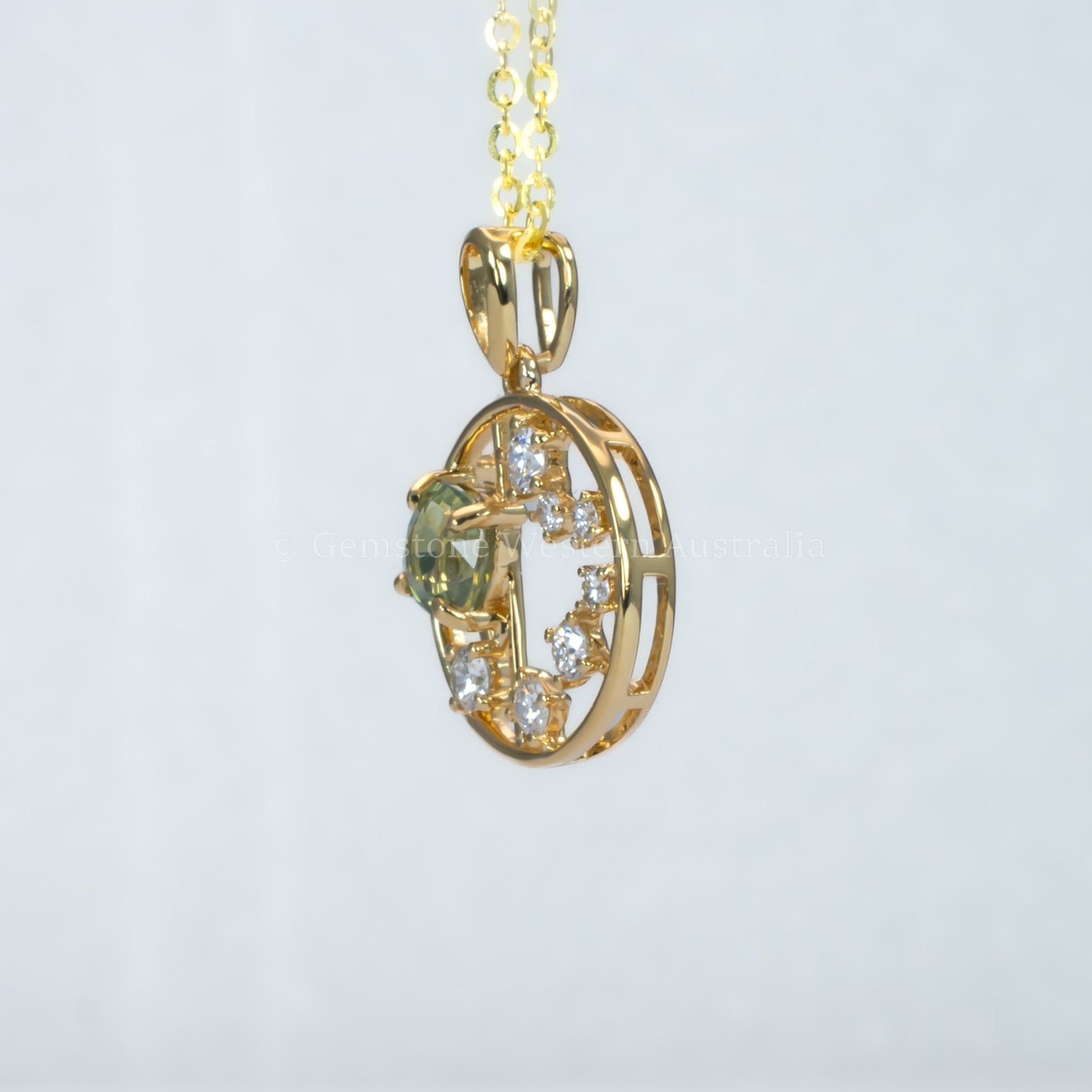 side view of open circle gold pendant with alexandrite gemstone and small diamonds on a light gray background