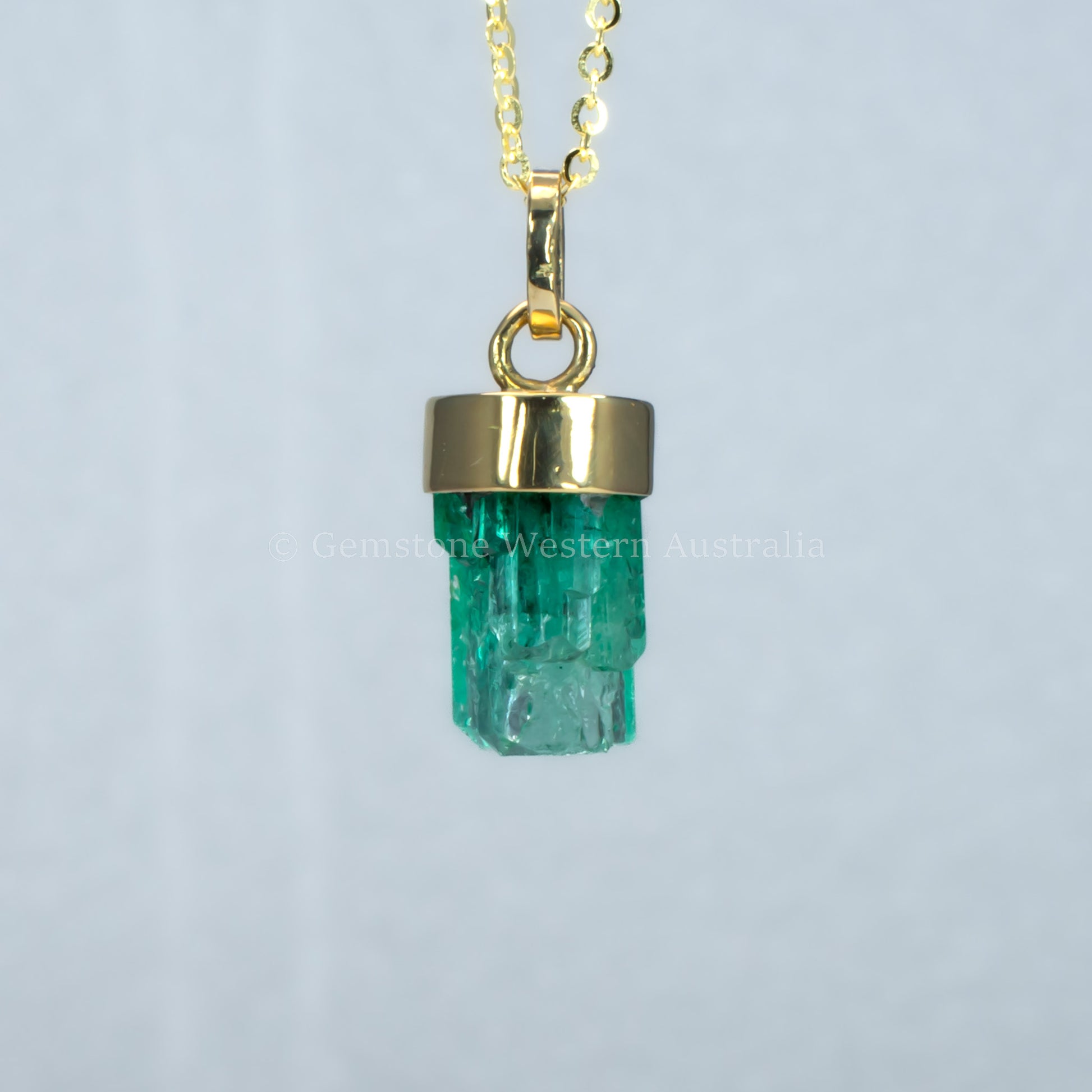 third perspective of Gold pendant with a rough emerald crystal on a light gray background