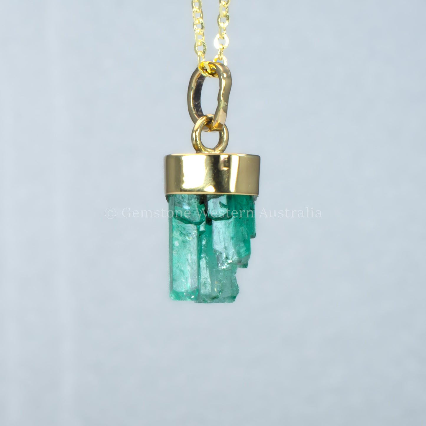 Gold pendant with a rough emerald crystal on a light gray background