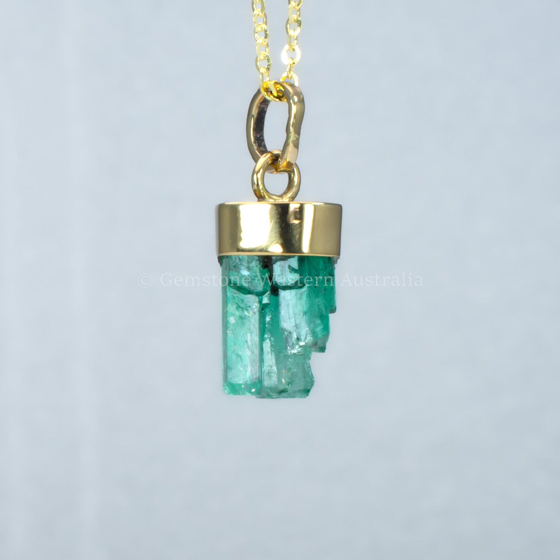 Gold pendant with a rough emerald crystal on a light gray background