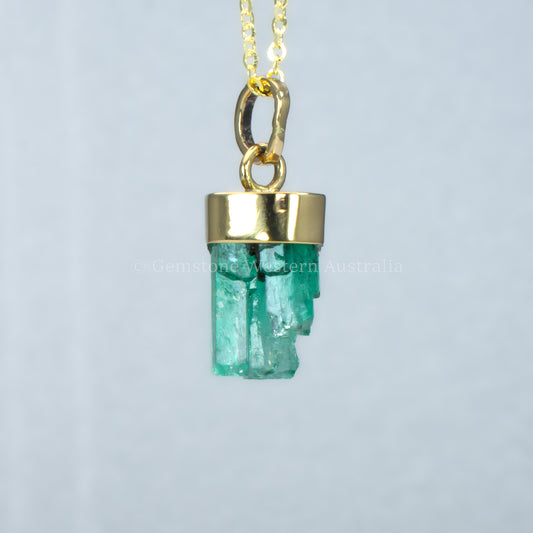 Gold pendant with a rough emerald crystal on a light gray background