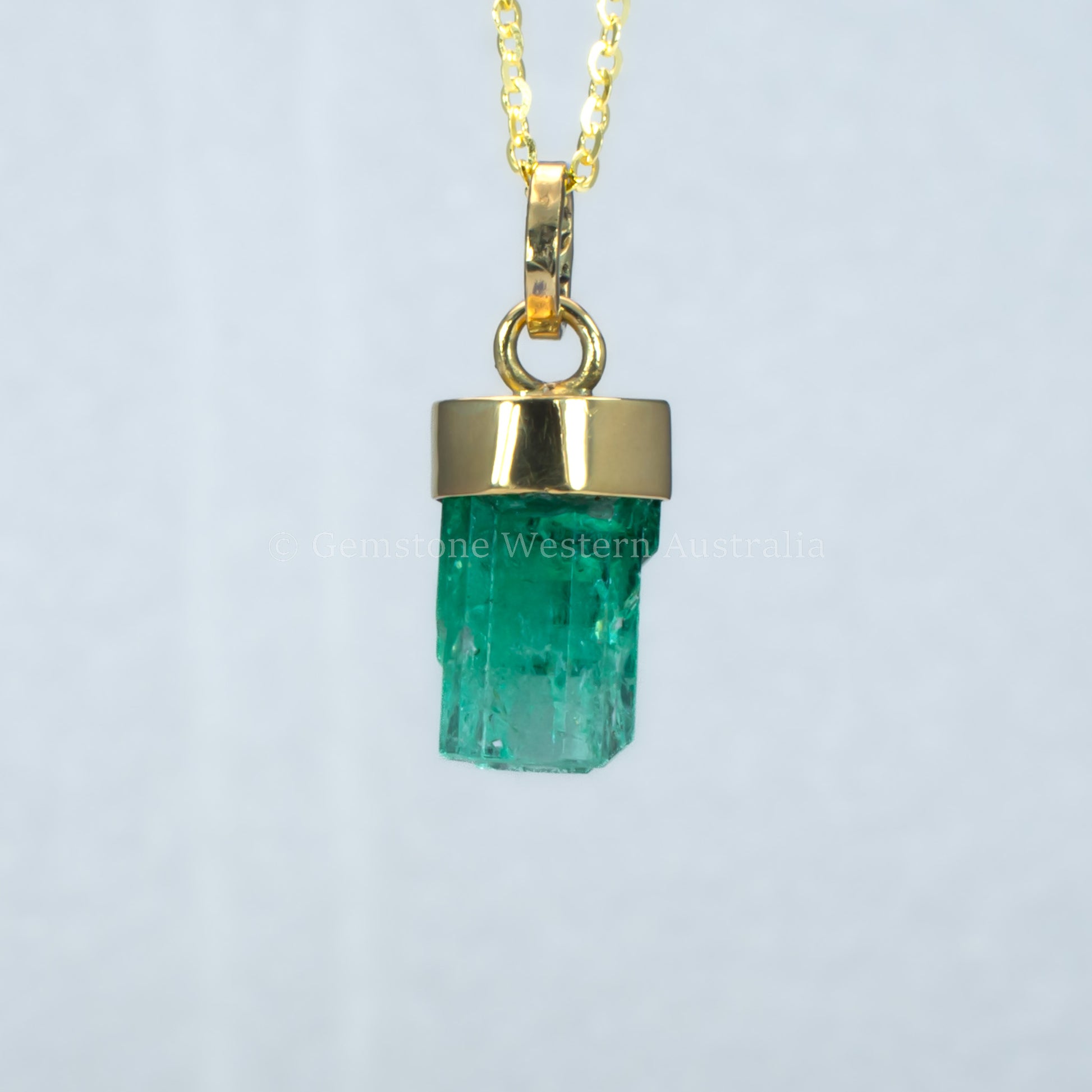 fourth perspective of Gold pendant with a rough emerald crystal on a light gray background
