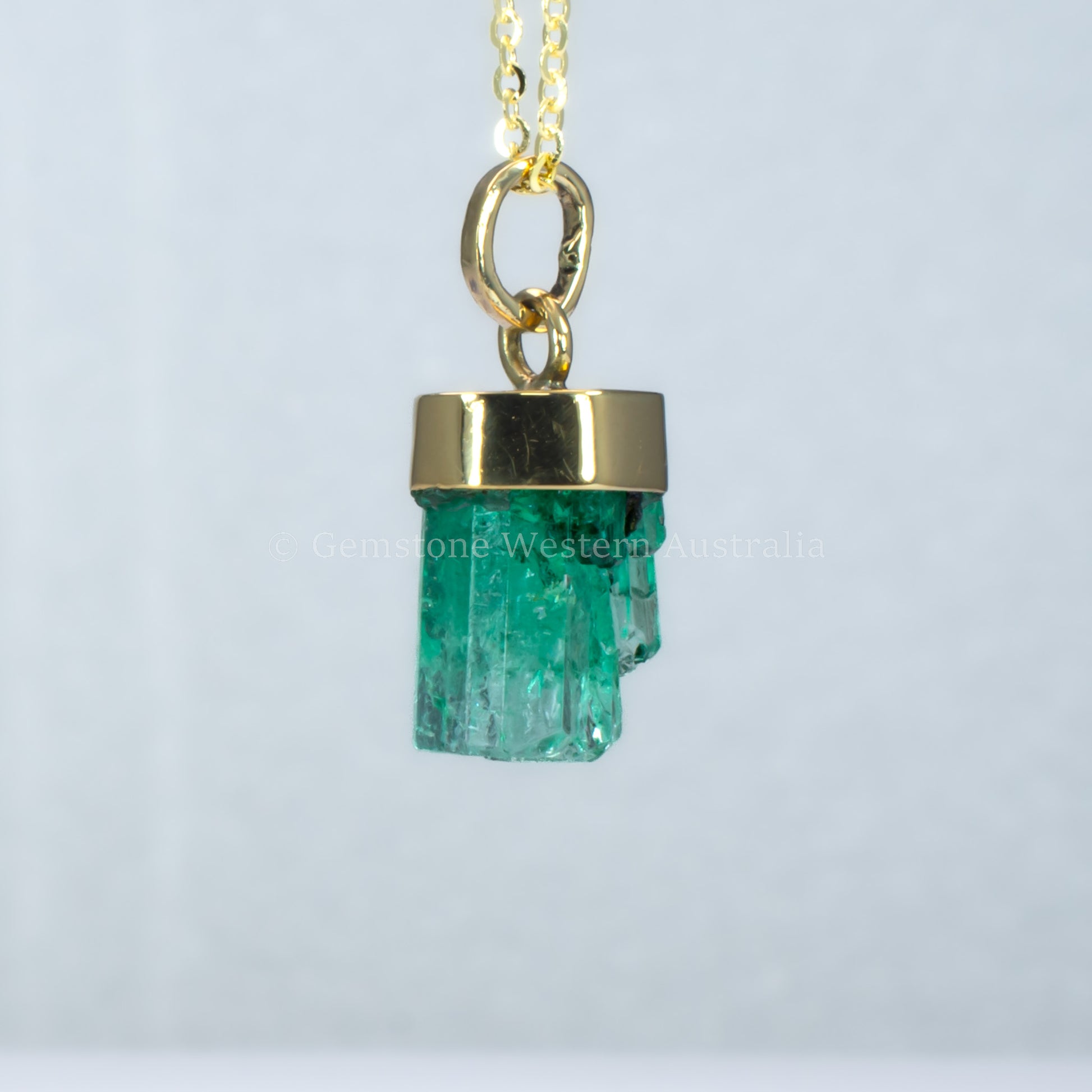 fifith perspective of Gold pendant with a rough emerald crystal on a light gray background