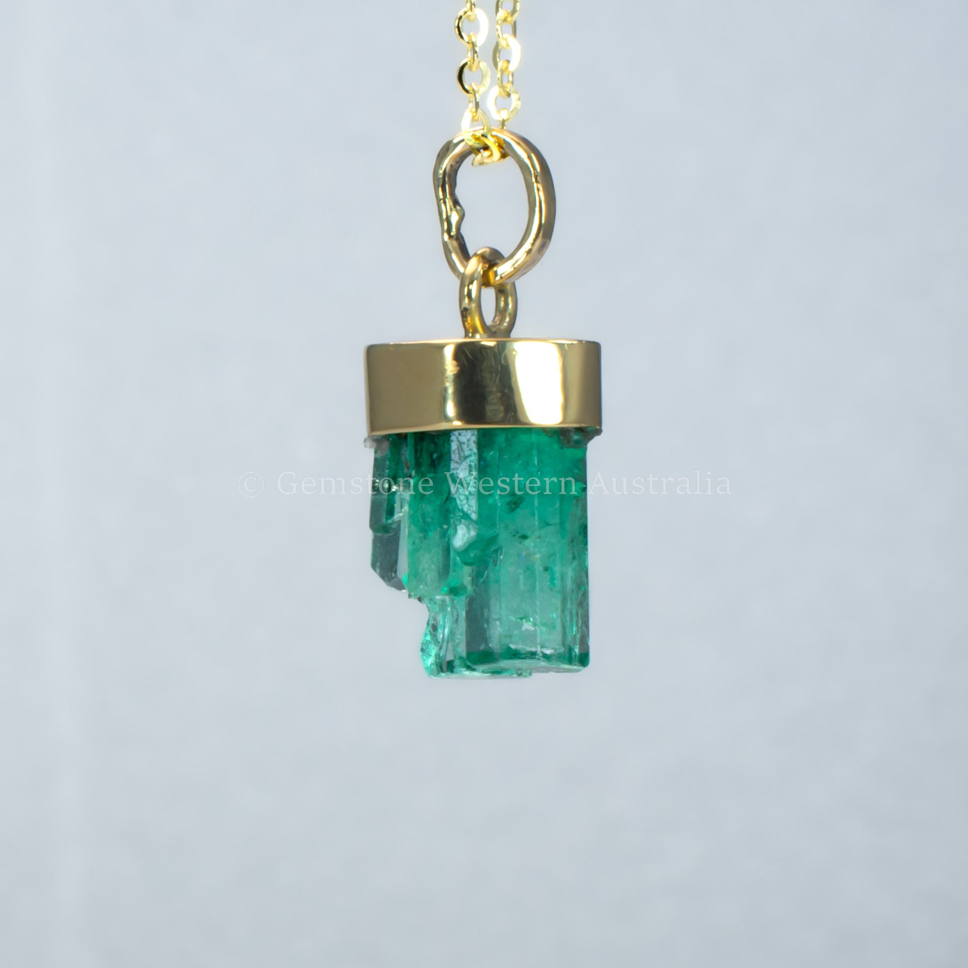 sixth perspective of Gold pendant with a rough emerald crystal on a light gray background