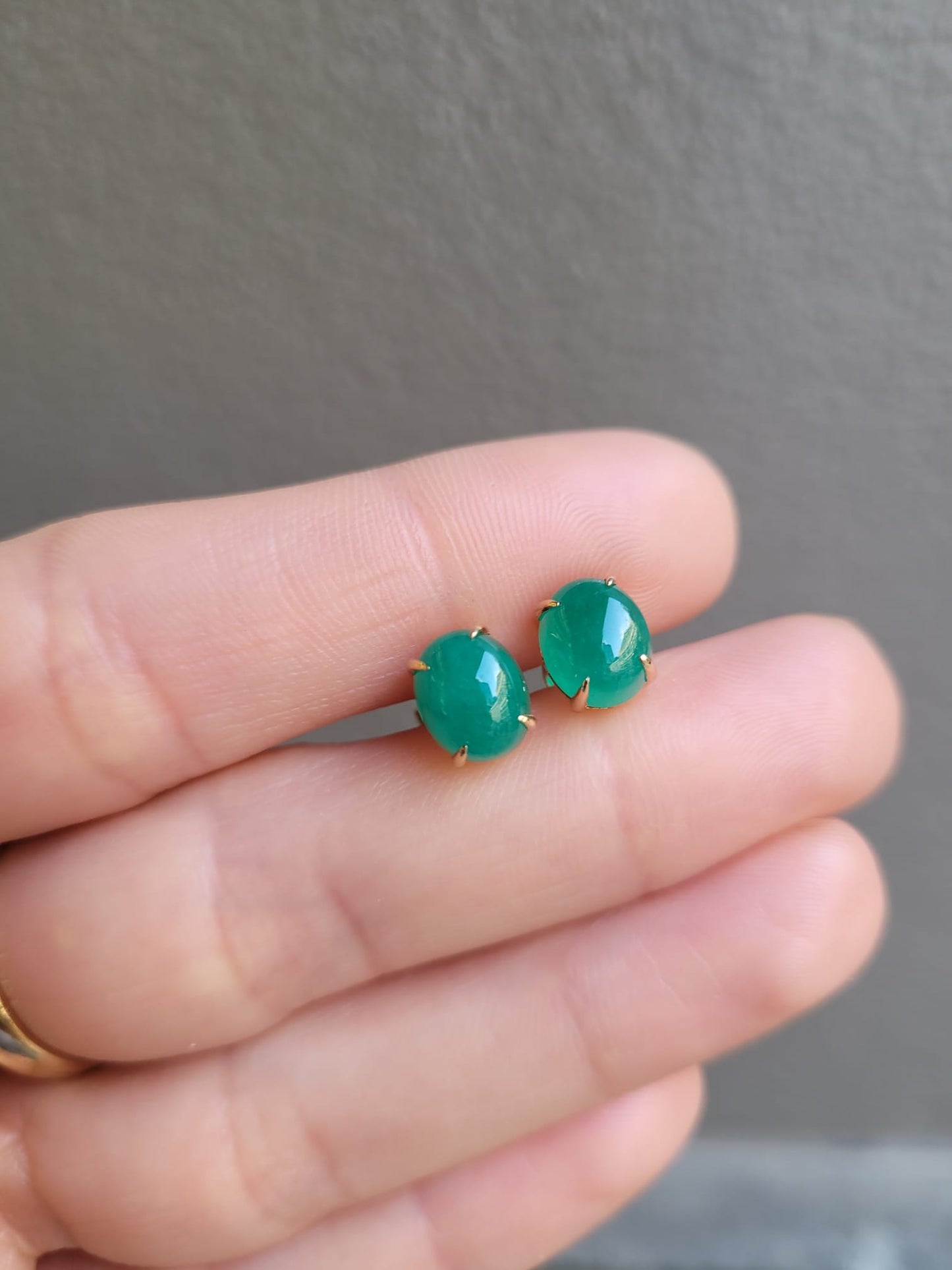 Cabochon emerald earrings held between fingers against a neutral background