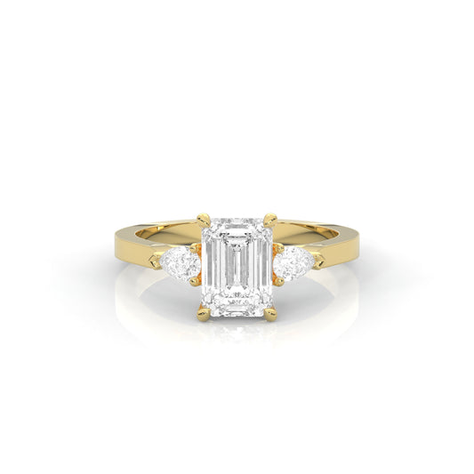 yellow gold ring with emerald-cut diamond and pear diamonds on the sides against a white background