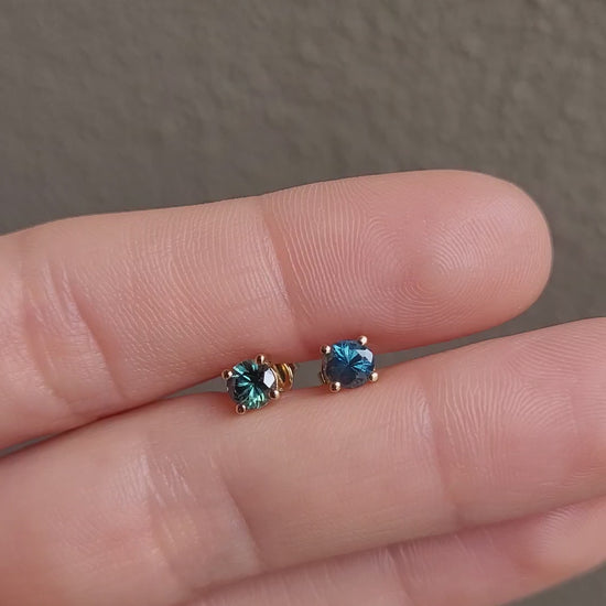 video of hand holding a pair of round natural Australian teal sapphire studs in neutral background