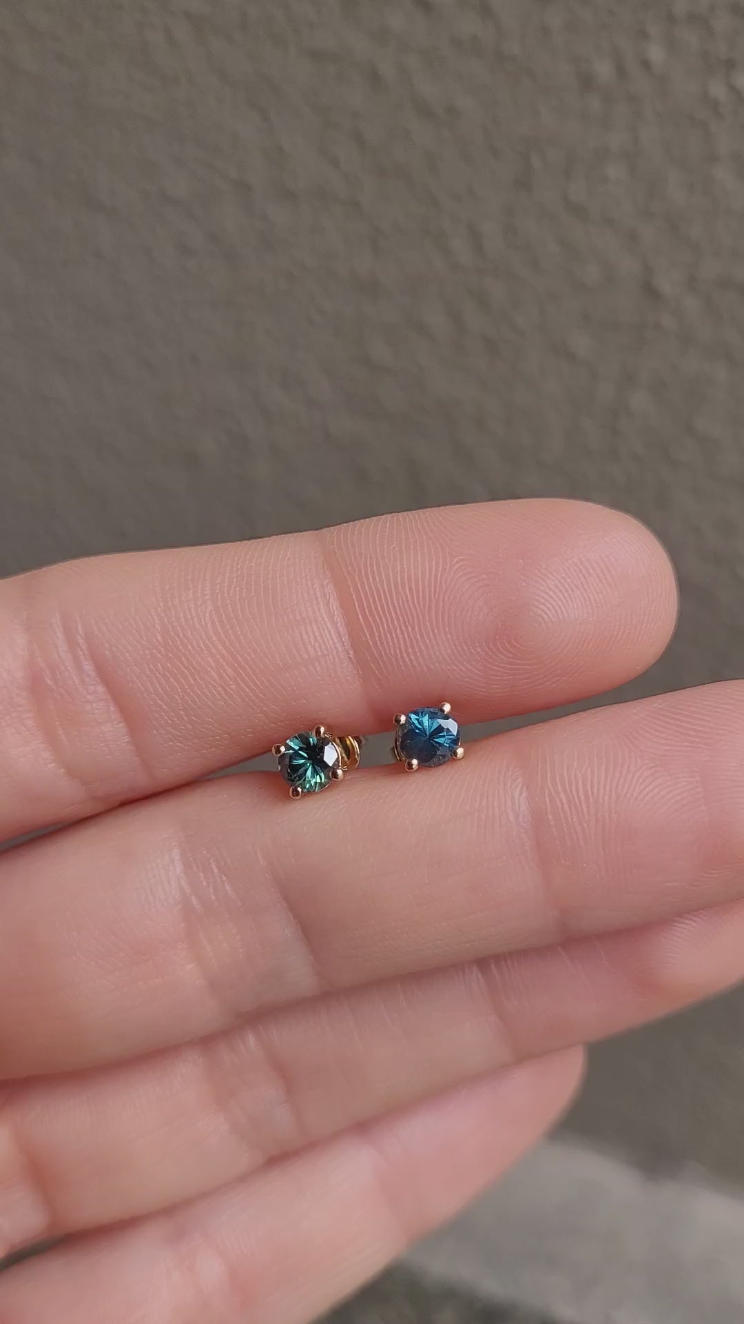 video of hand holding a pair of round natural Australian teal sapphire studs in neutral background