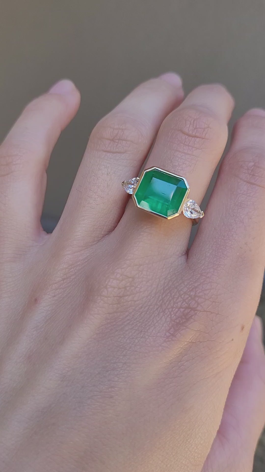 video of hand wearing a Colombian Emerald and Diamond Ring in 18K Yellow Gold – East West Emerald Cut in neutral background 