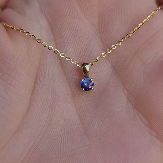 video of yellow gold royal blue sapphire pendant in gray background