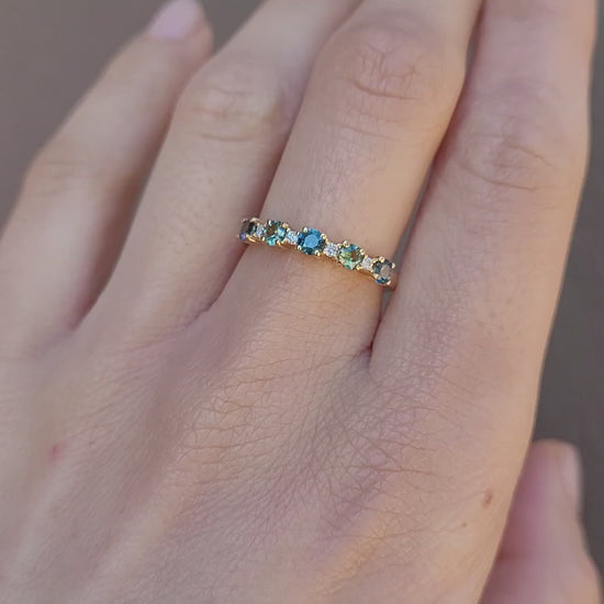 A video of a hand wearing a delicate half eternity band ring set with small Australian sapphires and diamonds against a neutral background