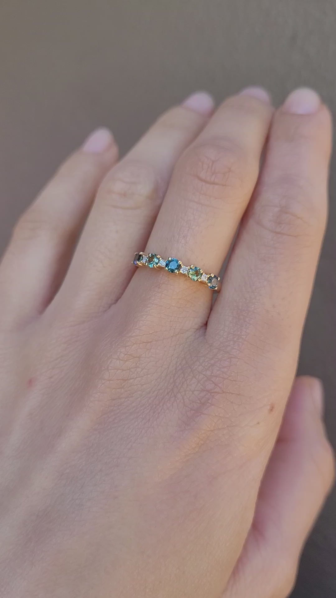 A video of a hand wearing a delicate half eternity band ring set with small Australian sapphires and diamonds against a neutral background