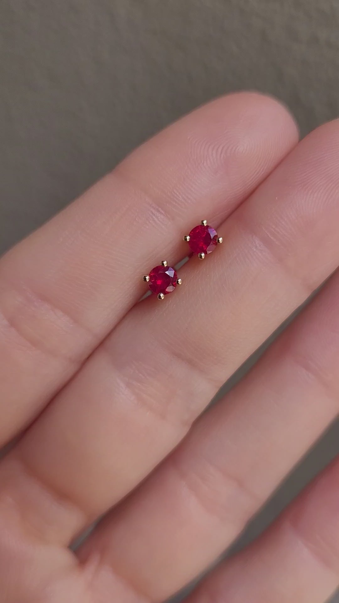 video of Natural Ruby Stud Earrings in 18K Yellow Gold held between fingers in neutral background