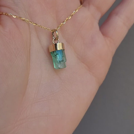 video of second perspective of Gold pendant with a rough emerald crystal on a light gray background