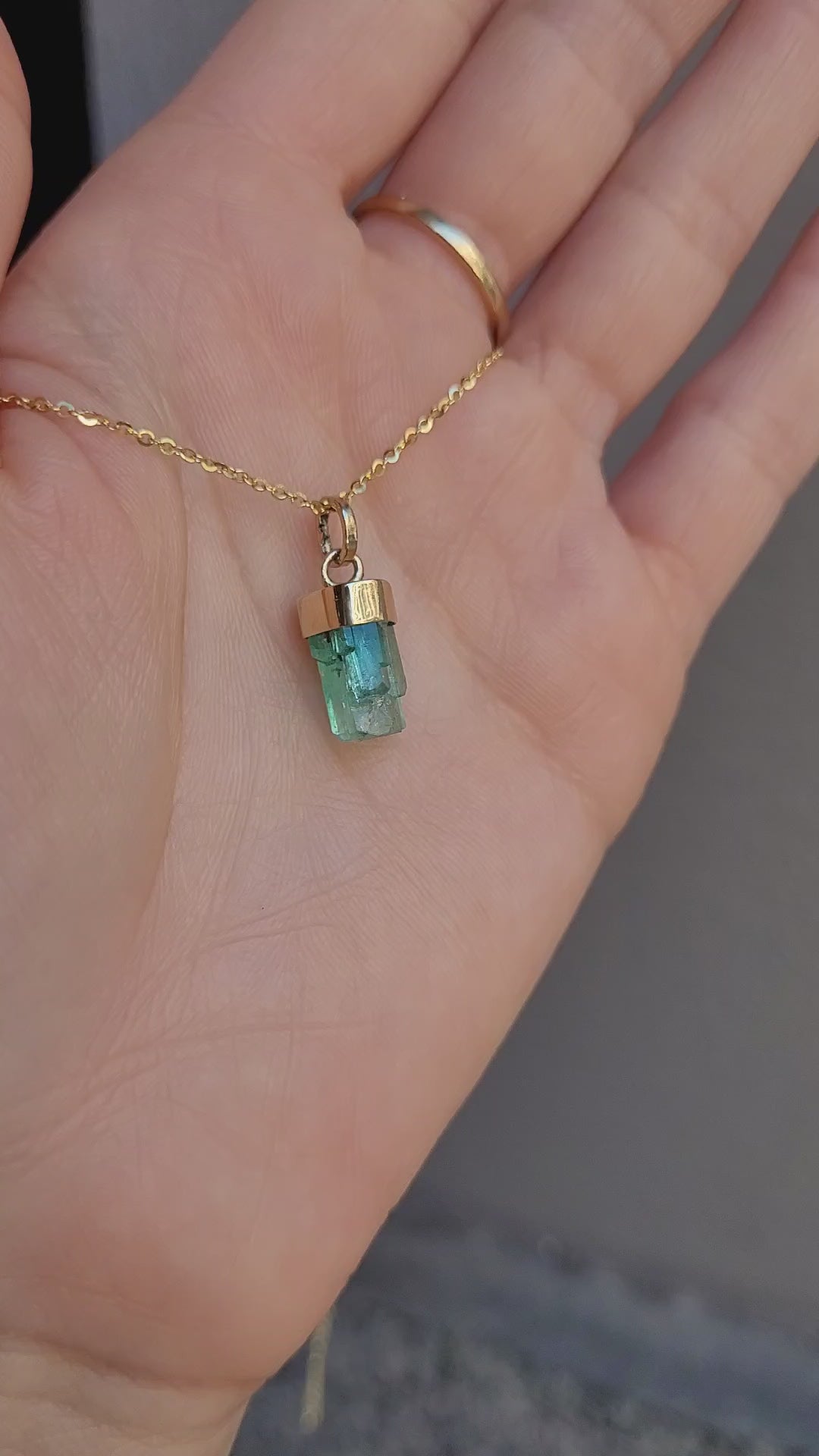 video of second perspective of Gold pendant with a rough emerald crystal on a light gray background
