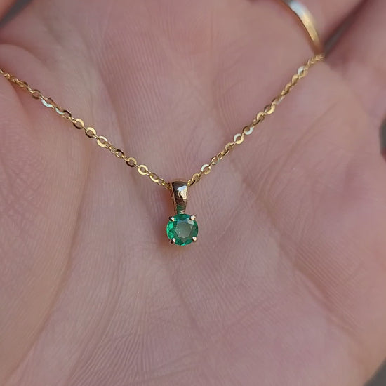 video on hand of petite emerald pendant in gold in gray background 