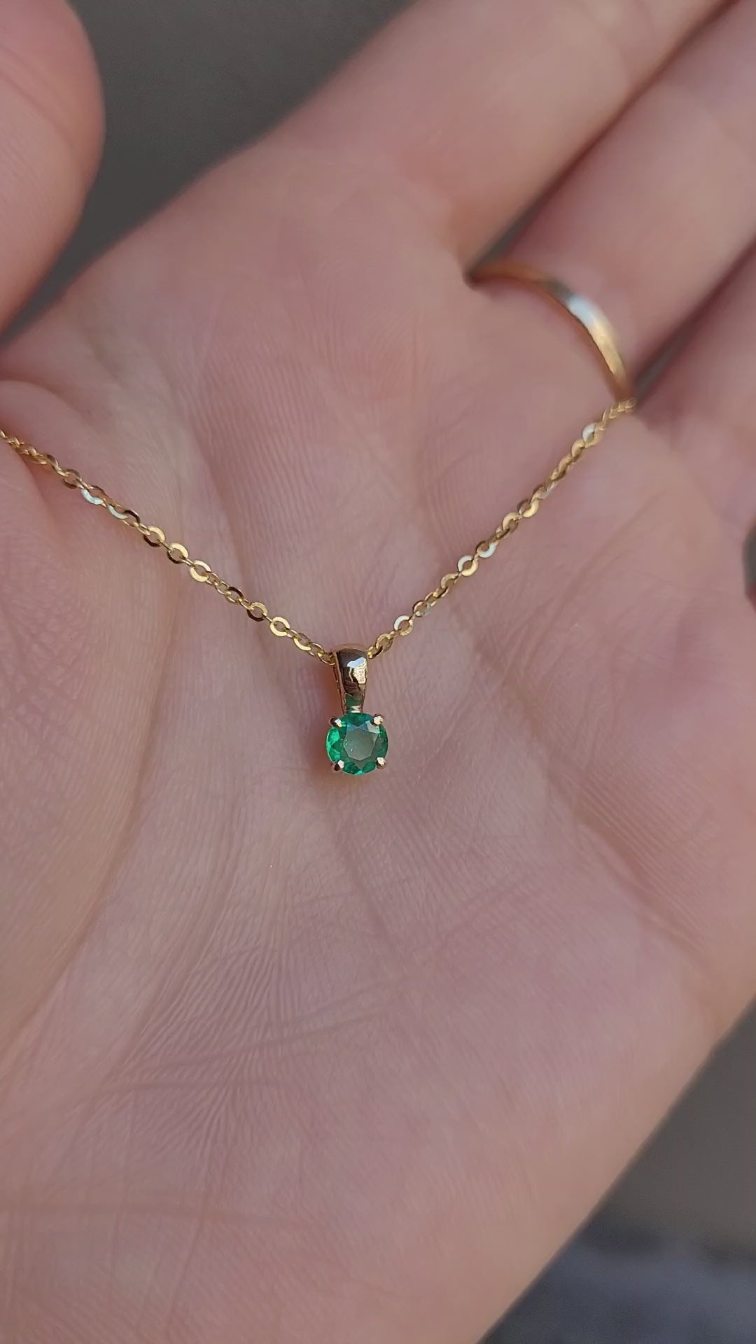 video on hand of petite emerald pendant in gold in gray background 