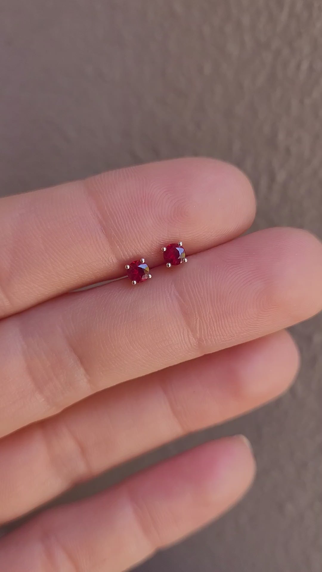 video of ruby earrings in platinum held between fingers against a neutral background