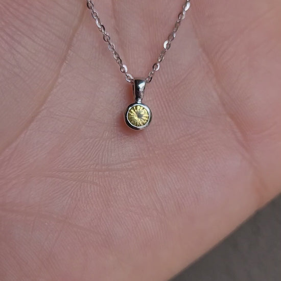 video of platinum pendant with yellow sapphire in a gray background