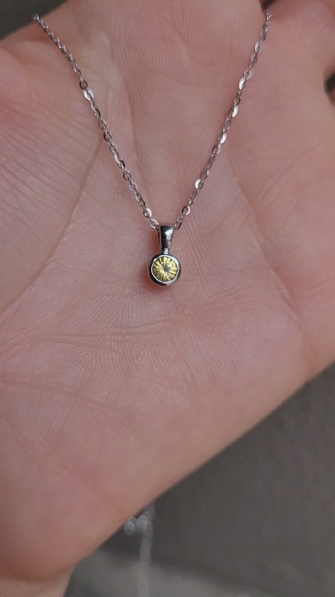 video of platinum pendant with yellow sapphire in a gray background