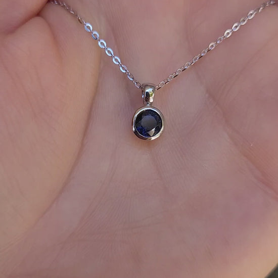 video on hand of platinum pendant with a blue sapphire on a gray background