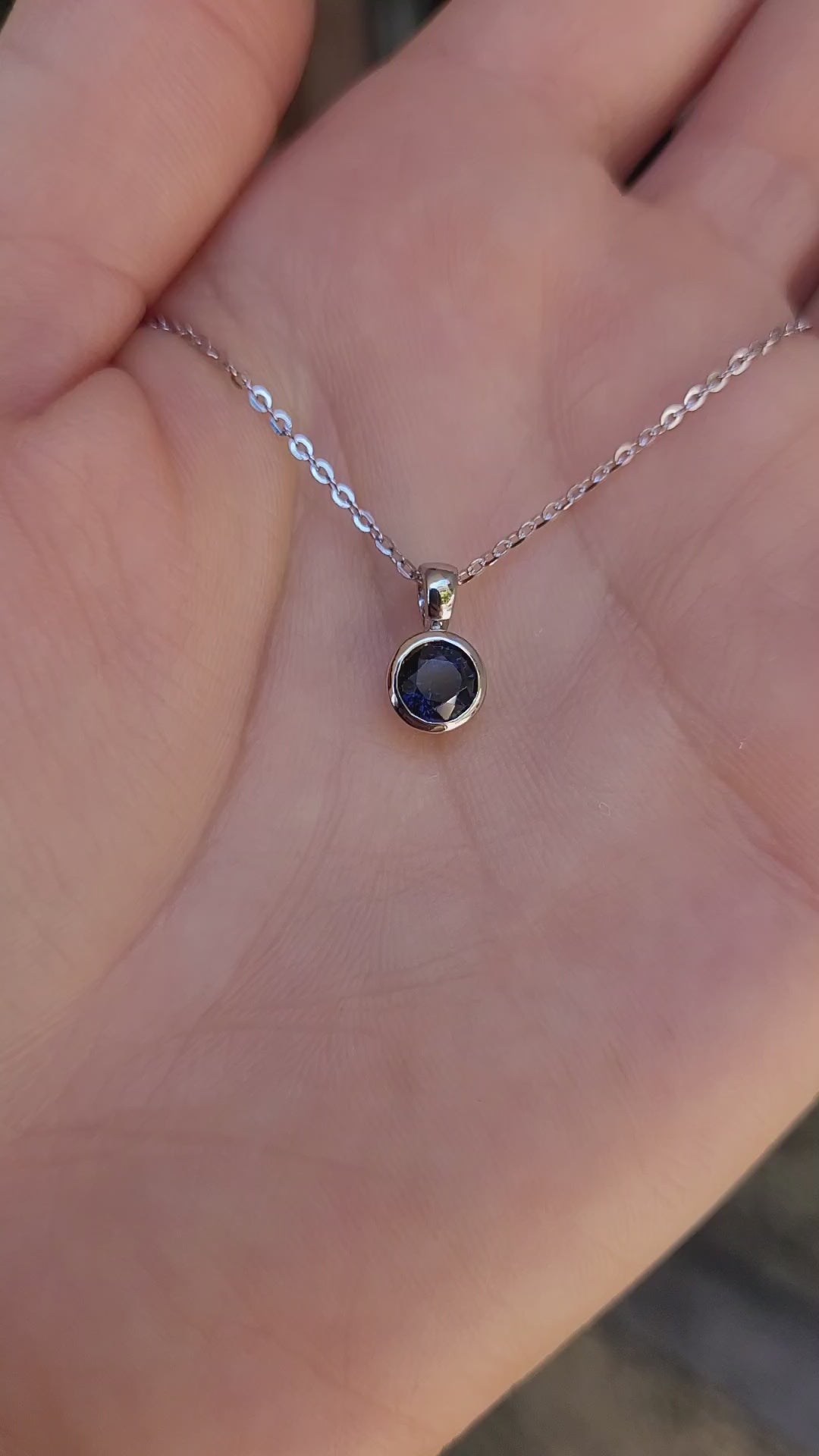 video on hand of platinum pendant with a blue sapphire on a gray background