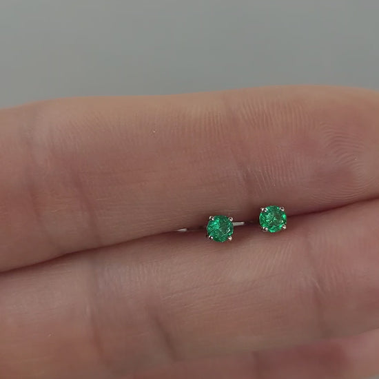 video of Pair of platinum stud earrings with emerald gemstones held on hand
