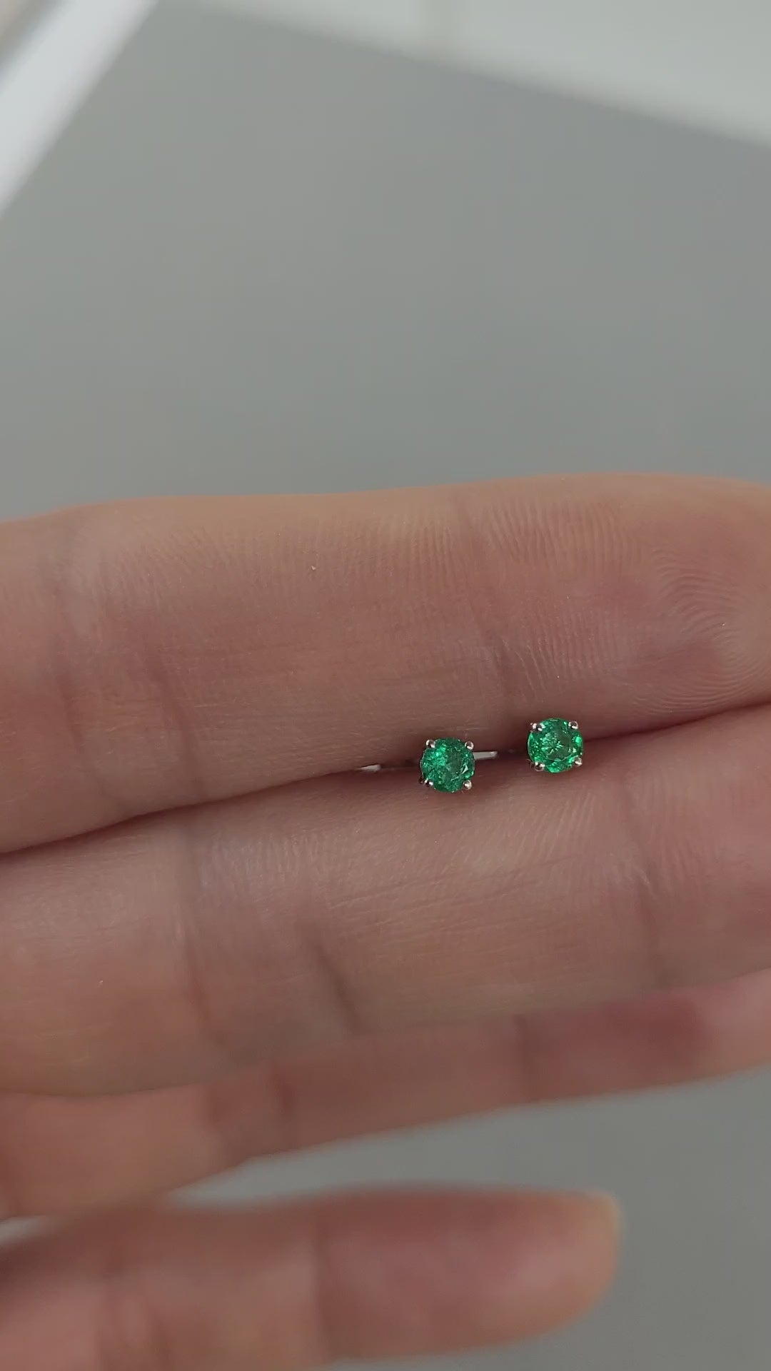 video of Pair of platinum stud earrings with emerald gemstones held on hand