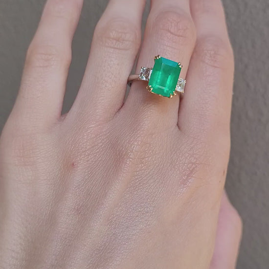 video of Hand wearing a Colombian Emerald and Diamond Ring in 18K Yellow Gold – East West Emerald Cut in neutral background