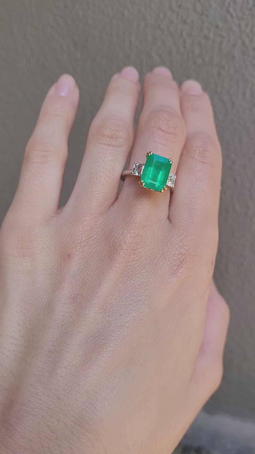video of Hand wearing a Colombian Emerald and Diamond Ring in 18K Yellow Gold – East West Emerald Cut in neutral background