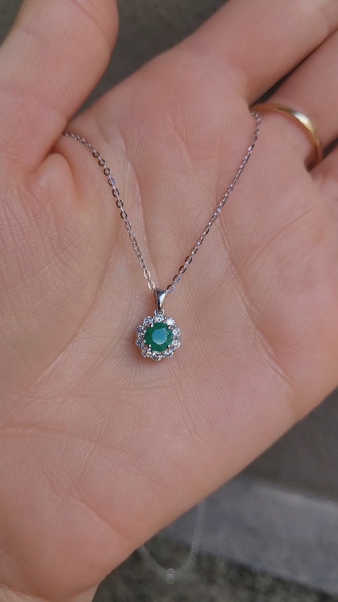 video on hand of Colombian emerald pendant on grey background 