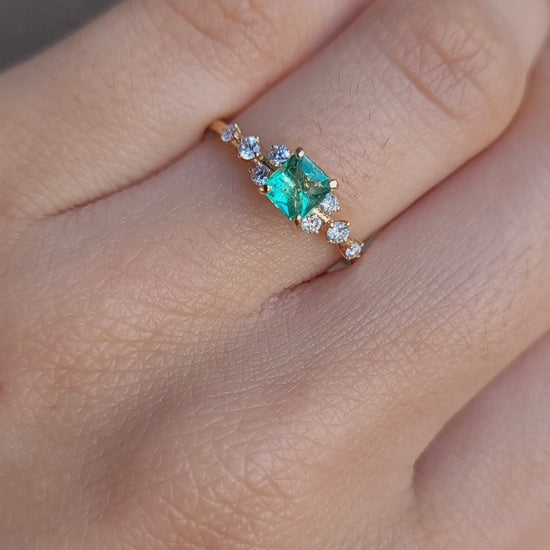 video on hand of Yellow gold ring with Colombian emerald and diamonds on gray background 