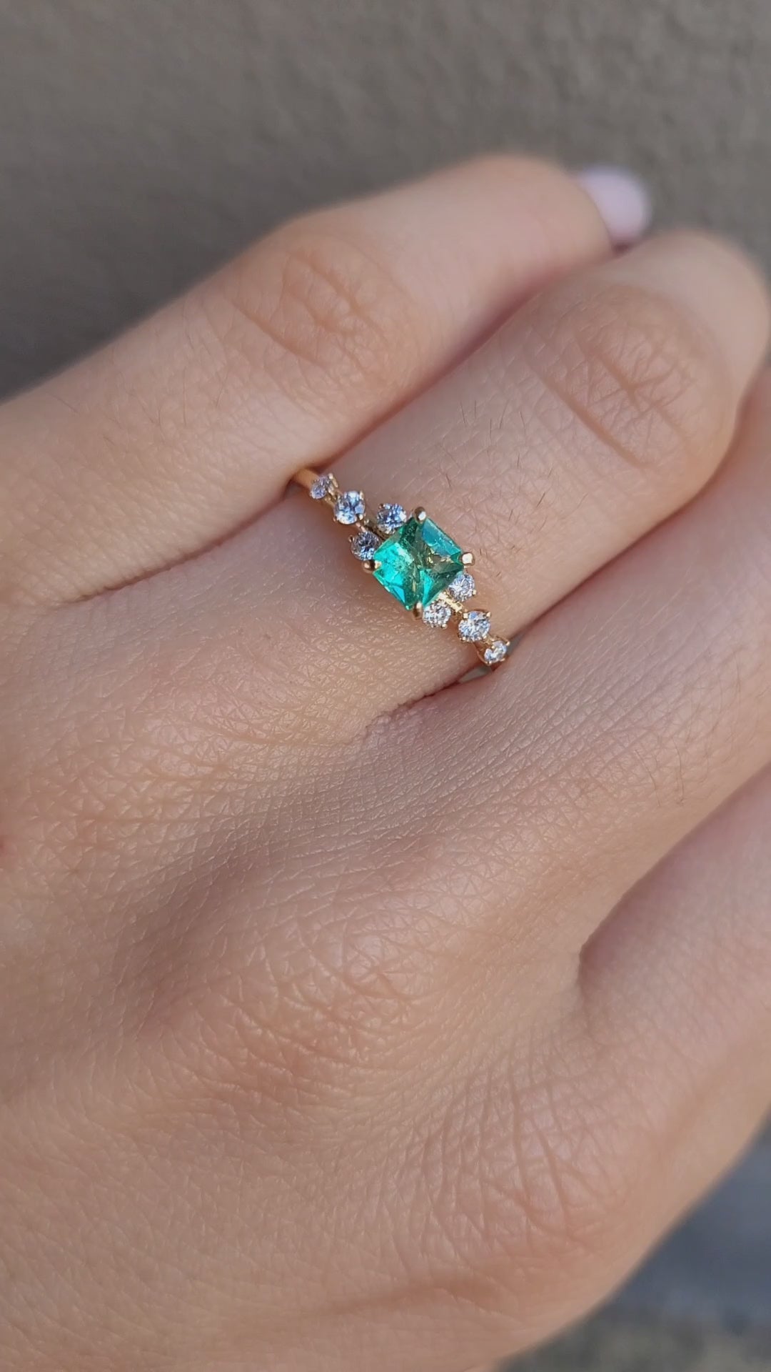 video on hand of Yellow gold ring with Colombian emerald and diamonds on gray background 